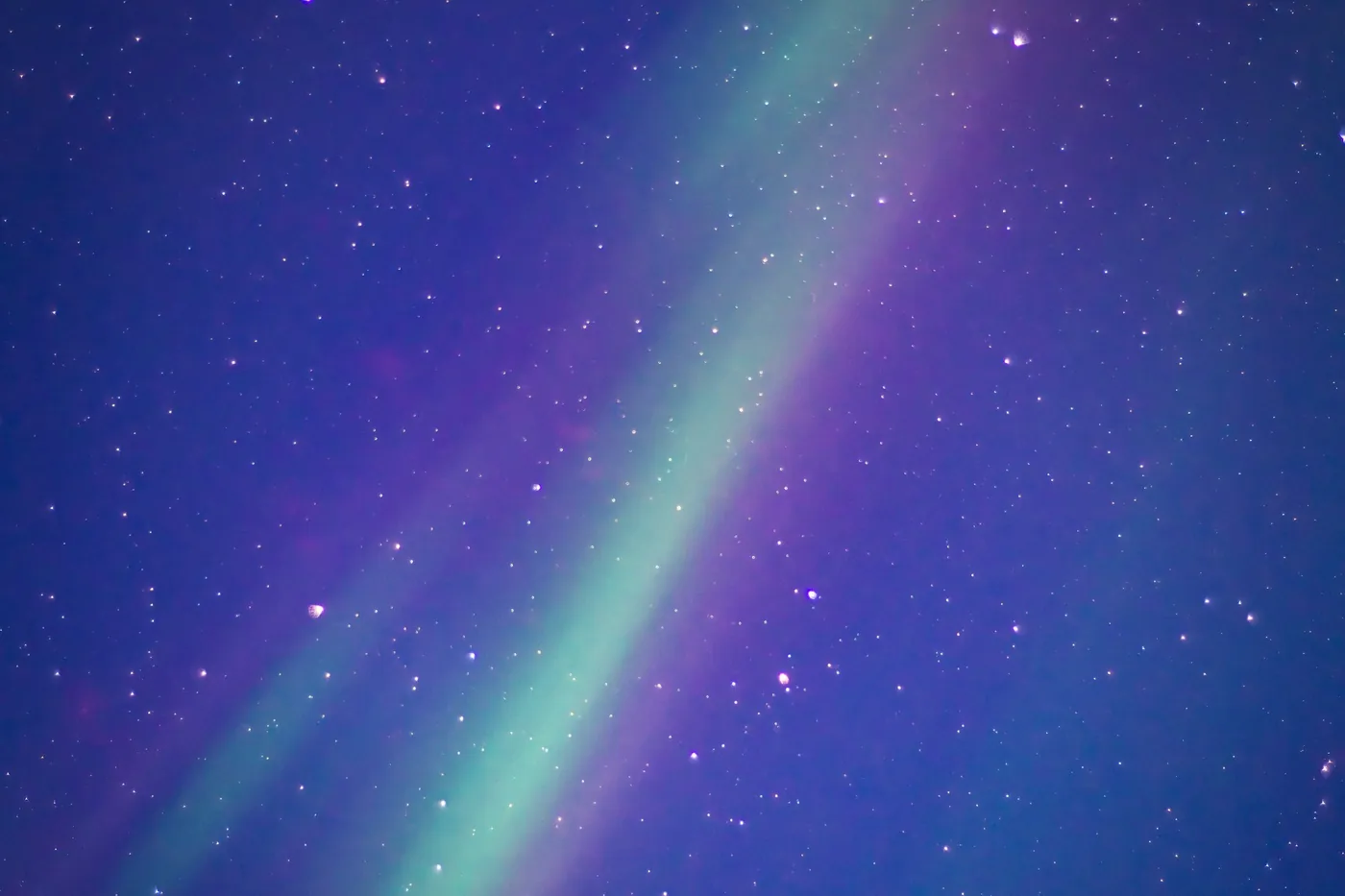 A broad band of green aurora with violet edges running diagonally across a dark blue sky full of stars